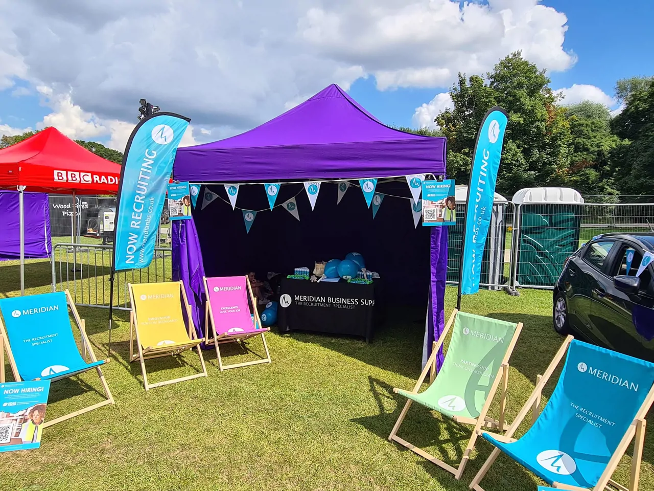 Tent and branded colourful deck chairs in a field for a local festival with branded flags