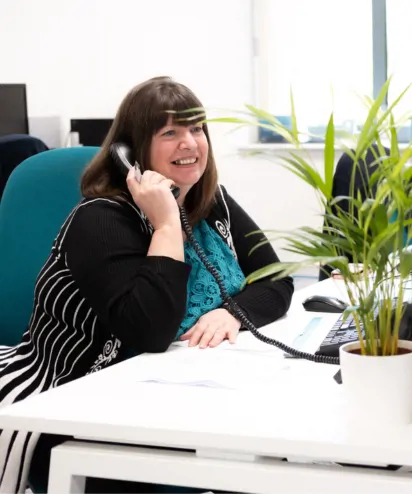 Woman picking up telephone at her desk in the office with plants around